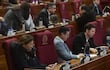 Fabiana Souto con chaqueta negra revisa su teléfono, mientras Cristing Villalba toma notas en un ambiente legislativo formal.