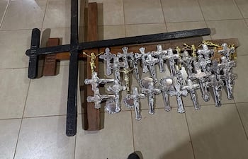 Conjunto de cruces de diferentes tamaños, incluyendo una grande negra y varias plata, en un entorno interior con paredes amarillas.