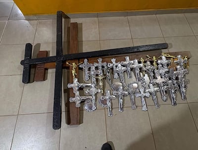 Conjunto de cruces de diferentes tamaños, incluyendo una grande negra y varias plata, en un entorno interior con paredes amarillas.