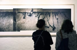 Dos mujeres de espaldas contemplan fotografías en blanco y negro en una galería iluminada suavemente.