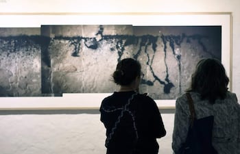 Dos mujeres de espaldas contemplan fotografías en blanco y negro en una galería iluminada suavemente.