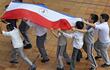 Niños de una escuela llevan en alto una bandera paraguaya. Foto del Observatorio Educativo Ciudadano.