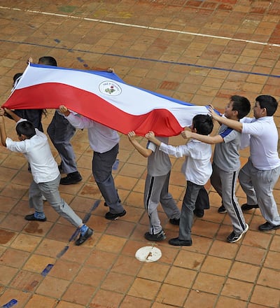 Niños de una escuela llevan en alto una bandera paraguaya. Foto del Observatorio Educativo Ciudadano.