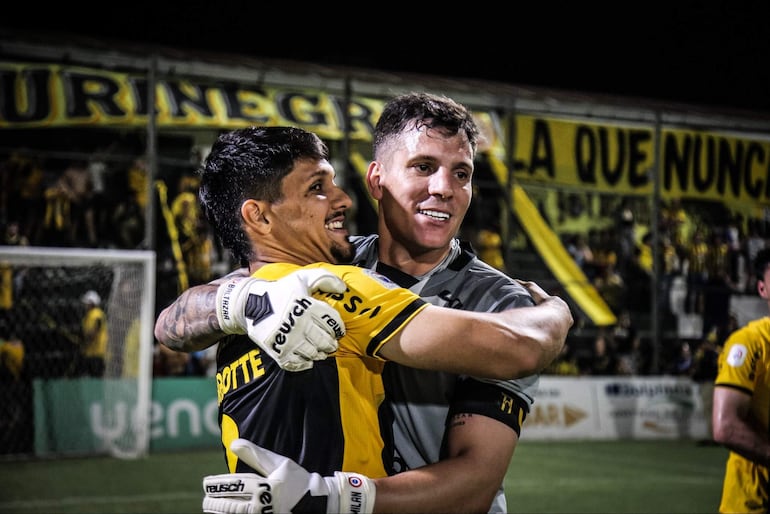Jugadores abrazados con camisetas amarillas y negras, expresiones de felicidad, en medio de un ambiente festivo en el estadio.