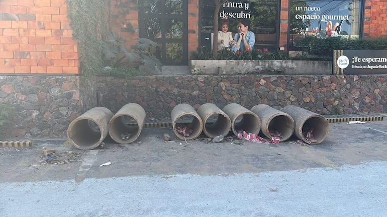 Ambiente urbano con tubos de concreto en el suelo y un cartel de un nuevo espacio gourmet.