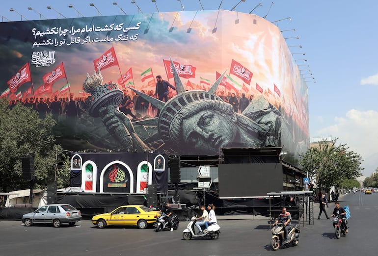 Iraníes pasan en coche junto a una valla publicitaria antiamericana en la plaza Enghelab, en el centro de Teherán (Irán). Persisten las tensiones entre Irán y Estados Unidos en torno al estrecho de Ormuz, mientras el presidente estadounidense, Donald Trump, anunciaba que las negociaciones tendrían lugar el 3 de agosto de 2026.
