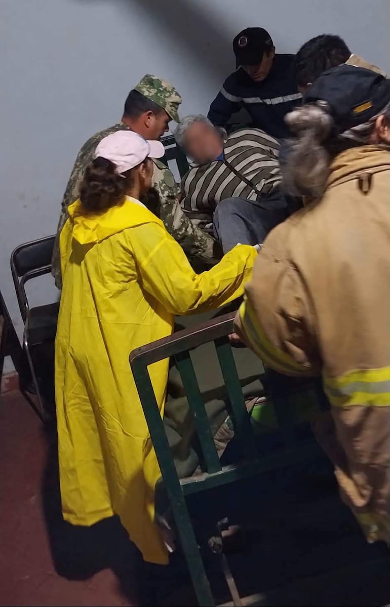 En la imagen se observa a un grupo de seis personas en un ambiente interior, posiblemente un centro de atención médica o un lugar de emergencia.
A la izquierda, una mujer con un vestido amarillo realiza una acción de asistencia. Junto a ella, un hombre de uniforme militar parece supervisar la situación. En el centro, un hombre mayor, con cabello canoso y una camiseta a rayas, se encuentra semi-reclinado, siendo asistido por las otras personas. A la derecha, un hombre vestido con una camisa de trabajo oscuro está inclinado hacia adelante, posiblemente observando o ayudando.
No hay elementos que identifiquen a un equipo de fútbol, ni lugares o estadios reconocibles. El ambiente refleja una situación de emergencia, con posibles acciones de atención médica en curso. No hay textos visibles ni otros objetos relevantes en el contexto noticioso.