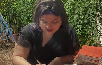 Lía Benítez Flecha, con cabello oscuro y blusa negra, concentra en firmar libros en un entorno natural.
