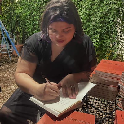 Lía Benítez Flecha, con cabello oscuro y blusa negra, concentra en firmar libros en un entorno natural.