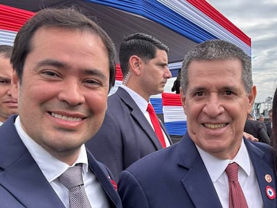 Rodrigo Gamarra y Jazmín Narvaez sonríen en eventos patrios, con fondo decorado en rojo, blanco y azul.