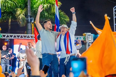 Dos hombres sonrientes levantan los brazos en señal de celebración, rodeados de banderas y un ambiente festivo en Ciudad del Este.