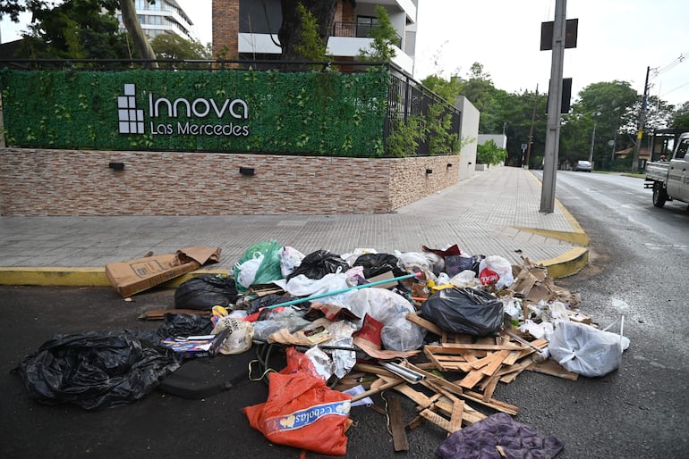 Basura en la calle frente al edificio Innova Las Mercedes, con árboles y un vehículo estacionado al fondo.