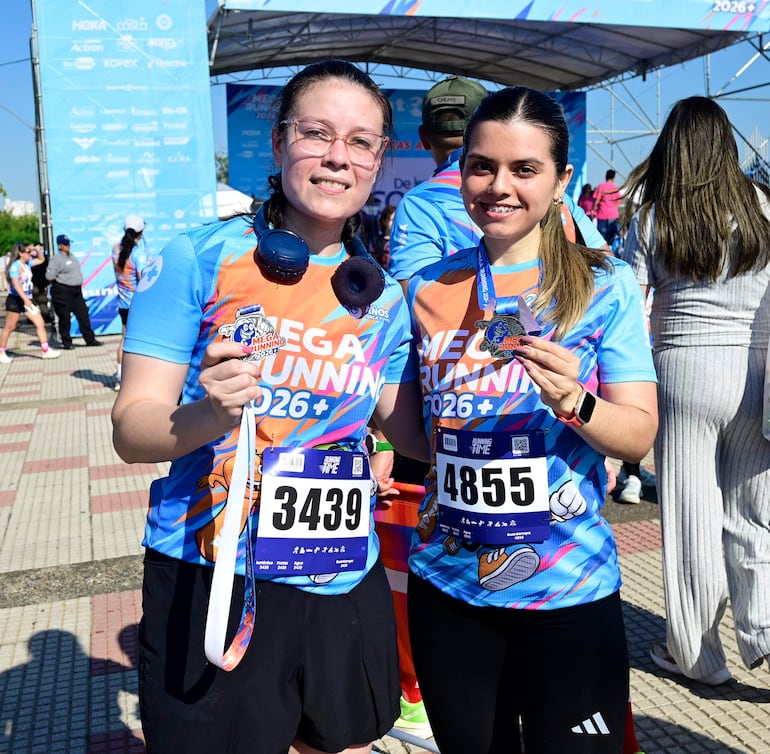 Mujeres con camisetas azules y medallas sonríen frente a la cámara en un evento de running, con el arco de meta al fondo.