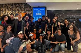 Grupo de aproximadamente 25 personas, algunas con camisetas negras, posando felices en un vestíbulo decorativo con el cartel 'BASURA'.