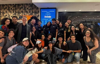 Grupo de aproximadamente 25 personas, algunas con camisetas negras, posando felices en un vestíbulo decorativo con el cartel 'BASURA'.