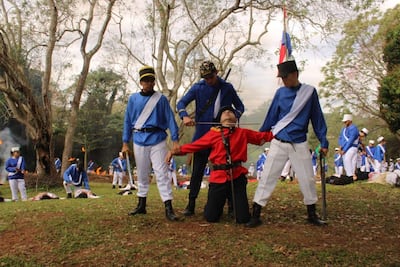 Hombres vestidos de azul y rojo, en un ambiente natural, representando una batalla, con posturas de confrontación.
