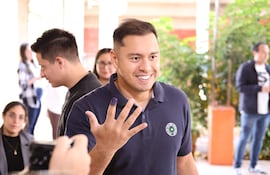 Daniel Pereira Mujica sonríe, en camiseta azul marino, con dedo índice marcado, rodeado de personas en un entorno natural.