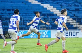 Alexis Cañete sonríe y levanta los brazos mientras celebra un gol, vestido con camiseta azul y blanca en un estadio.