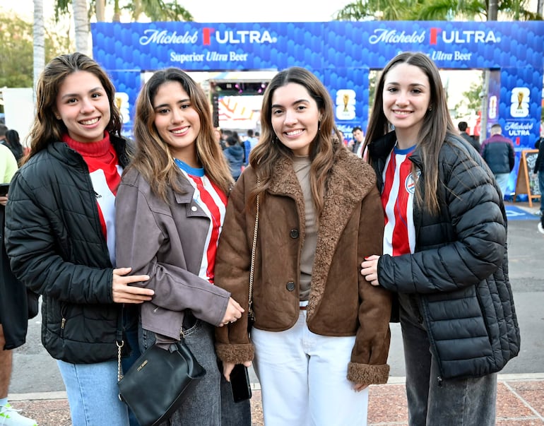 Cuatro mujeres sonriendo en un ambiente festivo, dos con camisetas del club Nacional, rodeadas de decoraciones de Michelob.