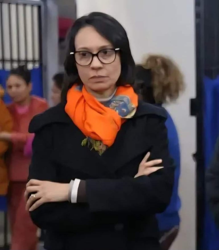 María Lidia Weyder con bufanda naranja y gafas, observando atenta a un grupo de mujeres en un interior colorido.
