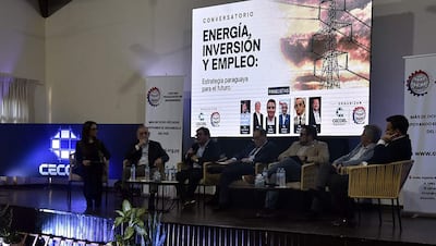 Seis panelistas en el conversatorio sobre energía, inversión y empleo, atentos en su atuendo formal, rodeados de un ambiente ordenado y banners informativos.