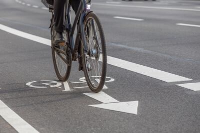 Un hombre pedalea una bicicleta por una bicisenda pintada en el asflato y señalizada con un dibujo de bicicleta y una flecha que indica el sentido del tráfico.