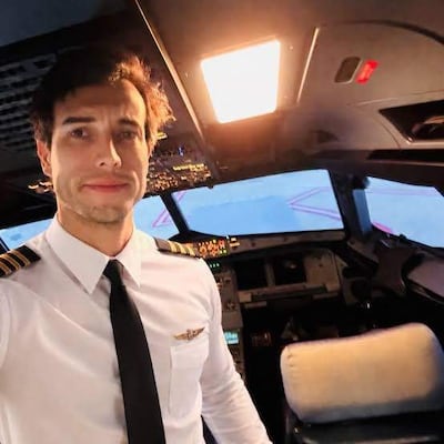 Leandro Bertazzo, piloto en cabina, viste camisa blanca con epaulettes y corbata negra, posando con instrumentos de vuelo en el fondo.