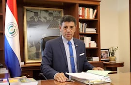 Víctor Ríos Ojeda vestido con traje oscuro y corbata azul, sentado en su oficina con expresión tranquila, junto a la bandera de Paraguay.