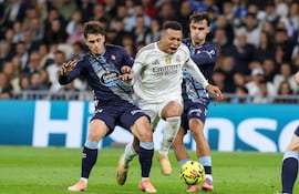 El delantero francés del Real Madrid, Kylian Mbappé (C), se escabulle entre el delantero español del Celta de Vigo, Pablo Durán (I), y el centrocampista español, Miguel Román, durante el partido de fútbol de la liga española entre el Real Madrid CF y el RC Celta de Vigo, en el Estadio Santiago Bernabéu en Madrid.