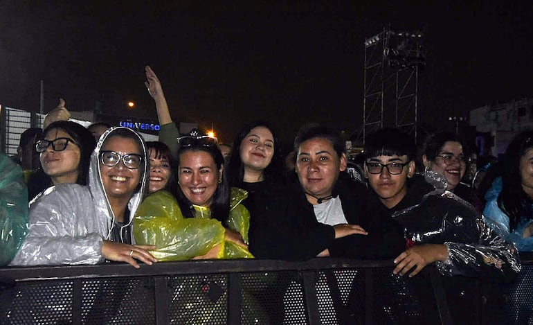 Seis personas sonrientes con ponchos en un ambiente festivo, disfrutando de un concierto al aire libre.