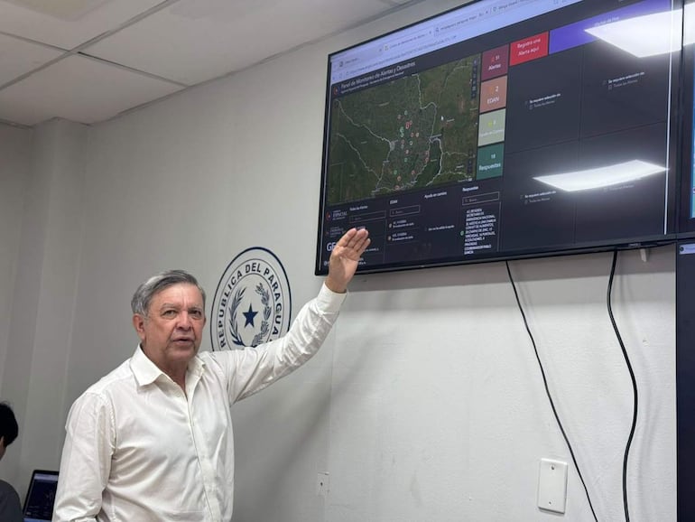 Arsenio Zárate, hombre canoso con camisa blanca, gesticula frente a un mapa en un ambiente oficial con escudo paraguayo.
