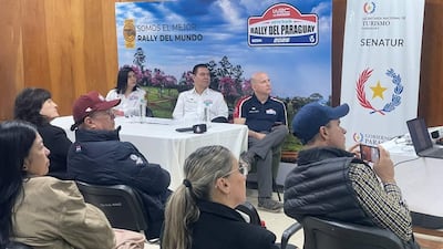 Jacinto Santa María, Alejandra Duarte y Antonio Carlos Barrios Fernández, atentos, lucen camisetas del rally en un evento decorado oficialmente.