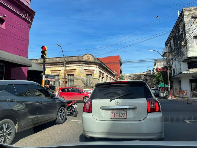 Intersección de calles con varios vehículos, semáforo rojo y edificio histórico al fondo.