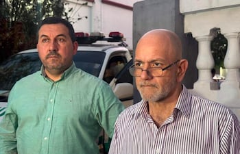 Silvio Alegre, con camisa verde, y Pablo Lemir, calvo con gafas y camisa de rayas, conversan seriamente junto a un vehículo de seguridad.o