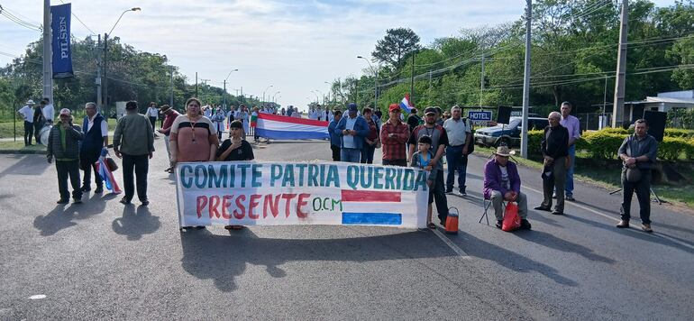 Grupo de personas en la calle con banner del Comité Patria Querida y un niño junto a un adulto, visiblemente involucrados en la protesta.