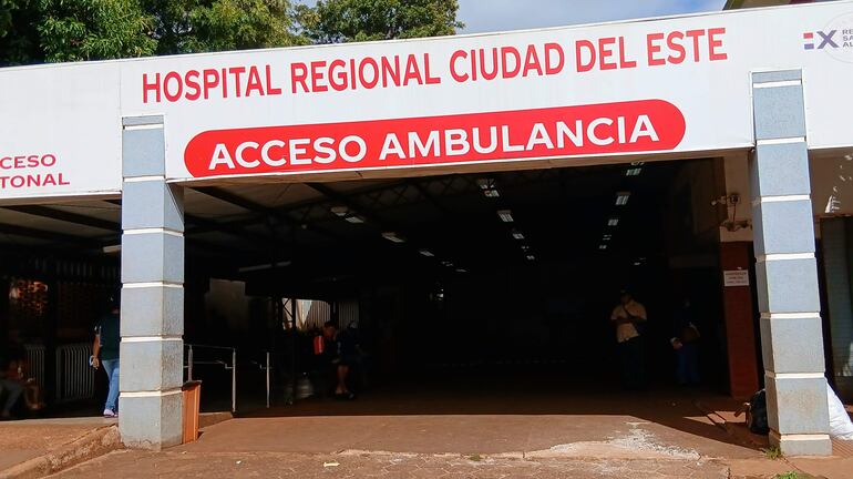 Entrada del hospital con letreros en rojo que indican 'ACCESO AMBULANCIA'. Espacio despejado sin personas visibles.