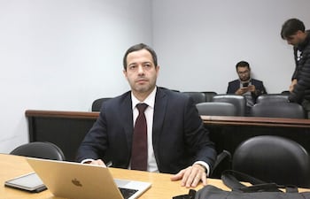 Francisco Cabrera en traje oscuro y corbata delgada, concentrado en su portátil, en un ambiente sobrio con otra persona al fondo.