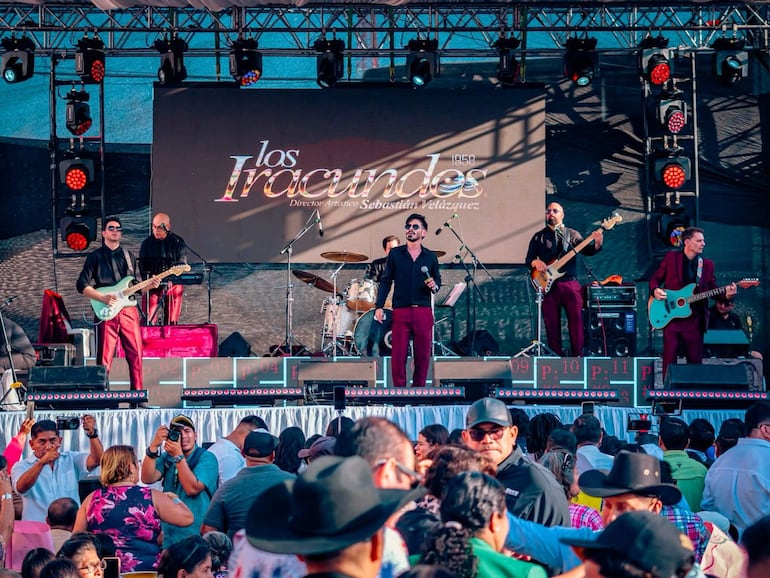 Cinco miembros de Los Iracundos en el escenario, vestidos de oscuro, mientras la audiencia disfruta del concierto festivo.