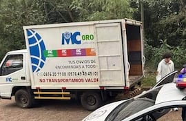 Camión de MC Group con persona vestida de blanco junto a policía en intervención, luces de emergencia activadas.