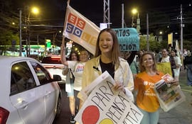 Soledad Nuñez, con blusa blanca, sostiene un cartel que dice 'PARA PENSÁ VOTÁ' en un ambiente urbano lleno de luces.