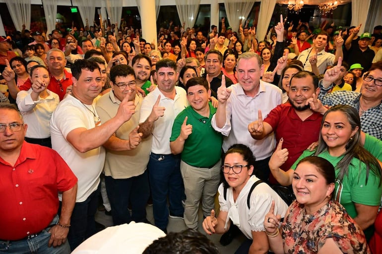 Gabriel Espínola rodeado de personas celebrando, todos con expresiones de alegría, en un salón decorado con colores vibrantes.