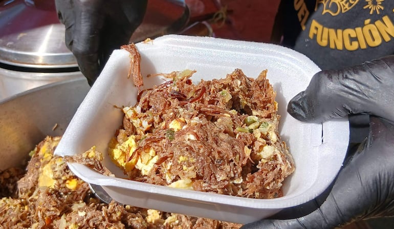 Plato de chatasca con ingredientes variados, preparado por un vendedor con guantes en un espacio al aire libre.
