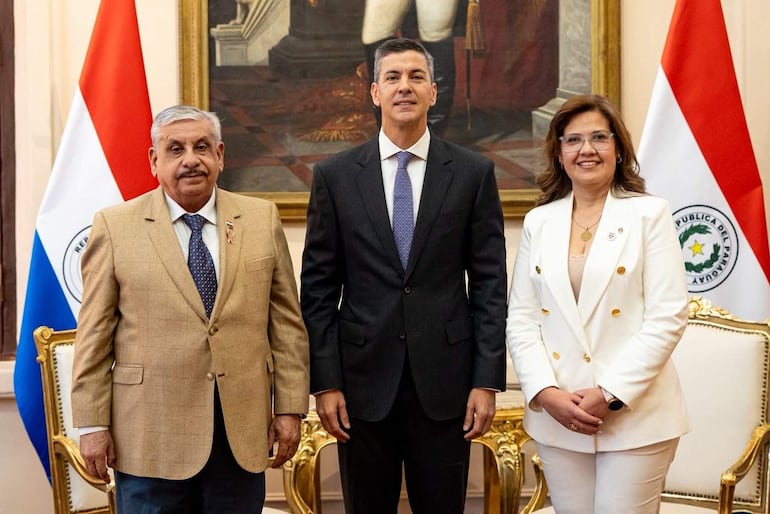 Cinthia Cardozo Nessi, en traje blanco, sonríe entre Santiago Peña y Isaías Fretes, en un entorno oficial decorado con banderas.