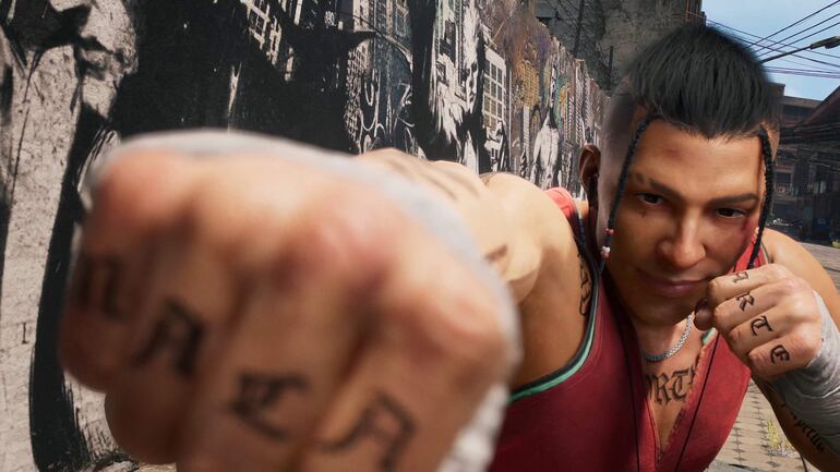 Joven con puño cerrado y tatuajes visibles, viste camiseta roja en un entorno urbano con grafitis de fondo.