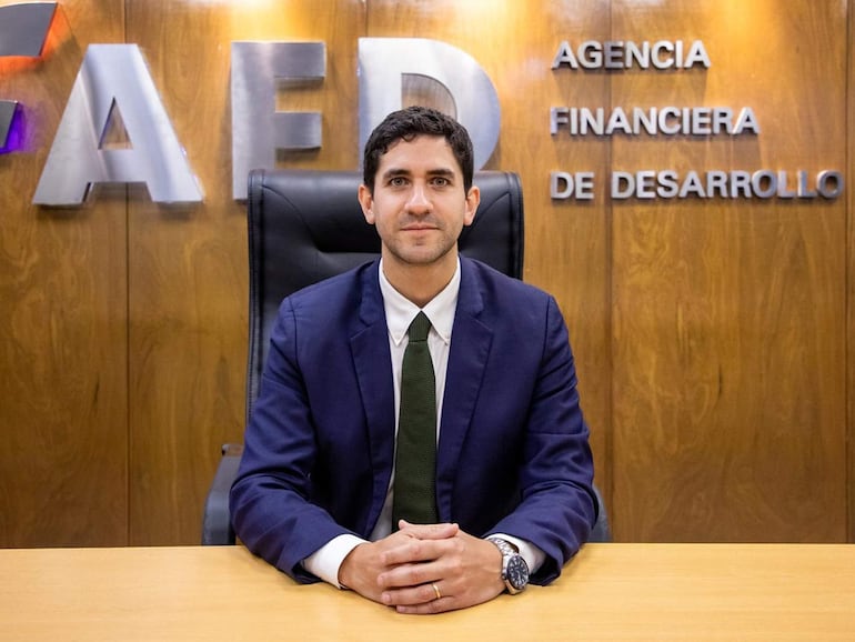 Ejecutivo en traje oscuro y corbata verde sentado en un escritorio, con expresión tranquila en un entorno institucional.