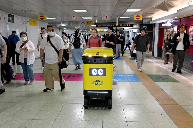 Personas caminan alrededor de un contenedor de basura robótico móvil que está siendo probado en el complejo de transporte de la estación de Shinjuku, en Tokio, el 18 de septiembre de 2026.