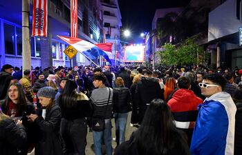 Hinchas de la selección paraguaya, con ropa oscura y banderas tricolores, se concentran frente a una pantalla en la calle Palma.