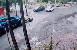 Agente caído en el asfalto en intersección urbana, mientras vehículos se desplazan alrededor, sin discernir emociones visibles.