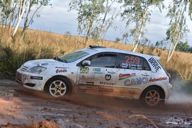 Automóvil Toyota sucio atraviesa barro en un paisaje rural, evidenciando su participación en competencias automovilísticas.