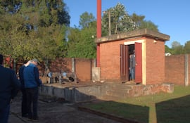 Cuatro personas de espaldas, observando un edificio de ladrillo en un entorno industrial con maquinaria de fondo y clima soleado.